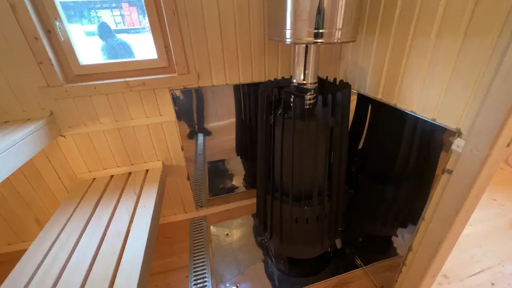Дровяная печь Grill'D Cometa Vega Long с заводскими экранами в парной готовой бани, рядом полки и слив в полу