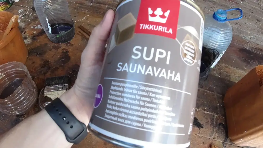 Банка Tikkurila Supi Saunavaha с защитным воском для деревянных поверхностей сауны, держит в руке