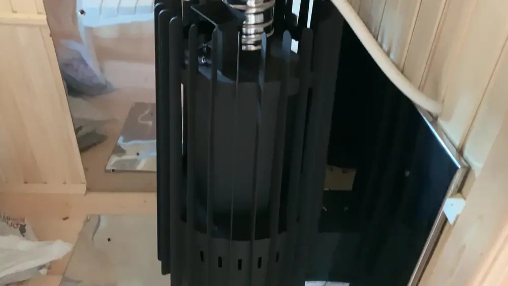 Печь Grill'D Cometa Vega Long в парной мобильной бани: чёрный корпус с вертикальными ламелями и стеклянной дверцей топки