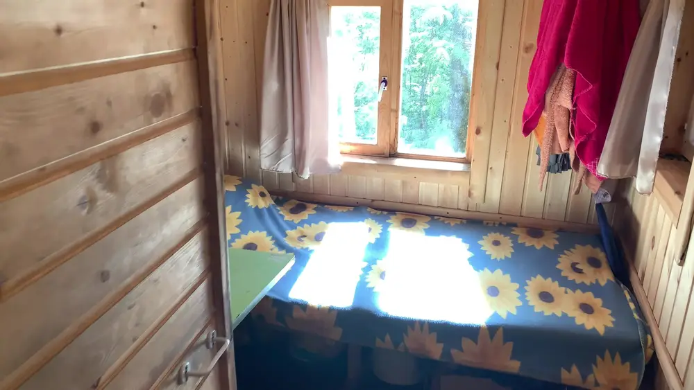 Кровать с покрывалом в подсолнухах в комнате отдыха каркасной бани под окном