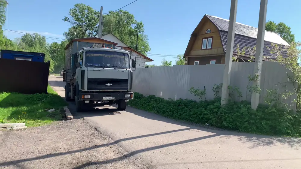 Двухосный МАЗ с готовой мобильной баней въезжает в узкую садоводческую улочку в Парголово под Санкт-Петербургом, на заднем плане столбы с проводами