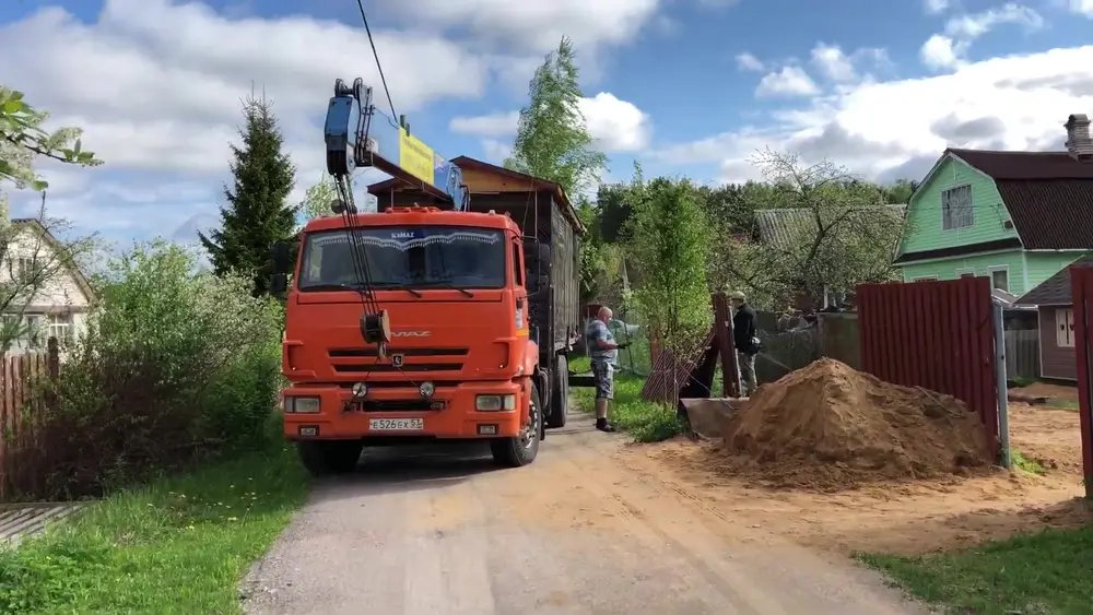 Манипулятор КамАЗ с готовой баней заехал на улицу заказчика в садоводстве, рядом песочная подсыпка для участка