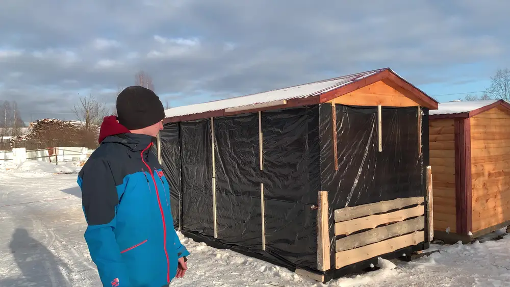 Готовая мобильная баня упакована в чёрную плёнку с вертикальными рейками и угловыми защитными брусками перед погрузкой